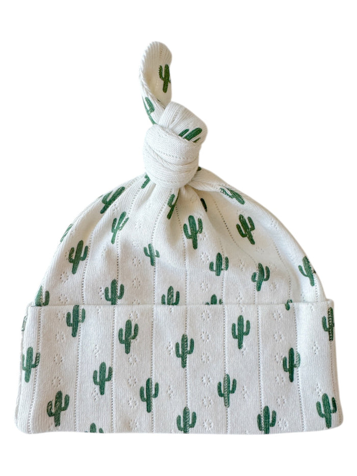 White baby hat with green cactus print and tied top knot design.
