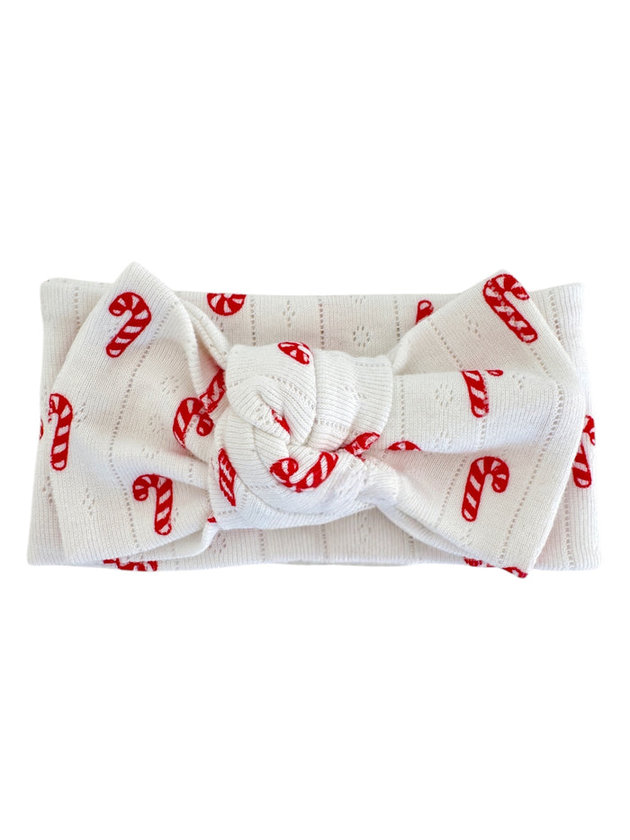 White headband with red candy cane pattern, featuring a knotted bow in the center.