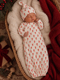 Newborn baby sleeping in a cozy basket, wearing a candy cane-patterned outfit and hat, surrounded by festive decor.