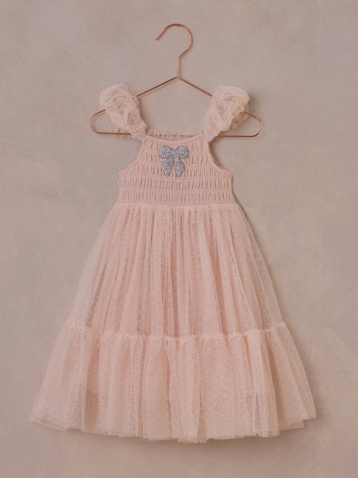 Pink tulle dress with ruffled sleeves and sparkly bow, hanging on a copper hanger against a neutral background.