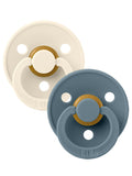 Two BIBS pacifiers in white and blue with gold accents on a light background.