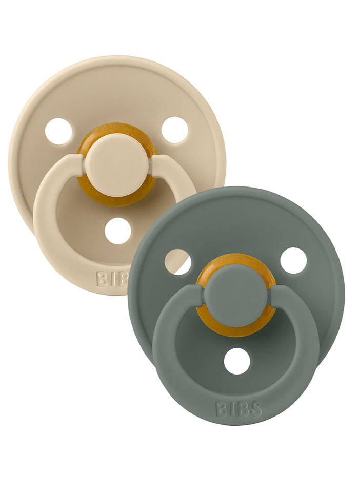 Two baby pacifiers in beige and green, featuring a round design with a central knob and the brand name "BIBS."