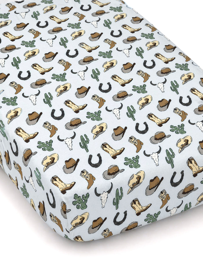 Light blue crib sheet featuring a western pattern of boots, hats, cacti, horseshoes, and cow skulls.