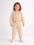 Smiling child in a floral-patterned outfit with sneakers, standing against a light background.