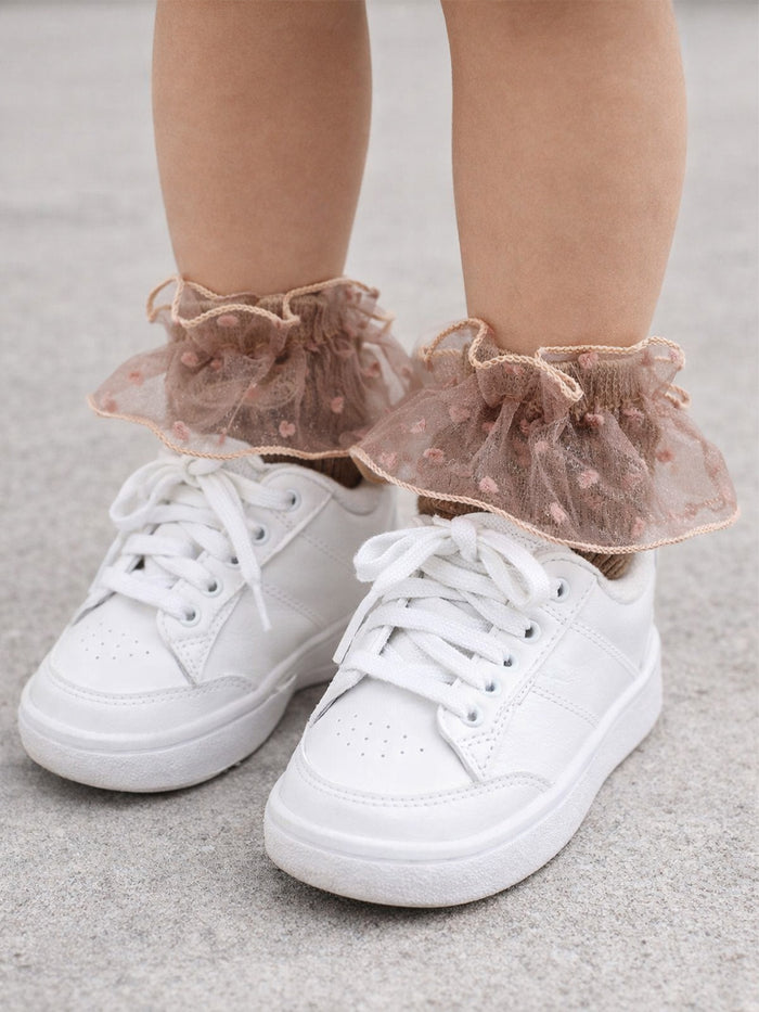White sneakers with frilly, pink heart-patterned ankle socks on a child's feet.