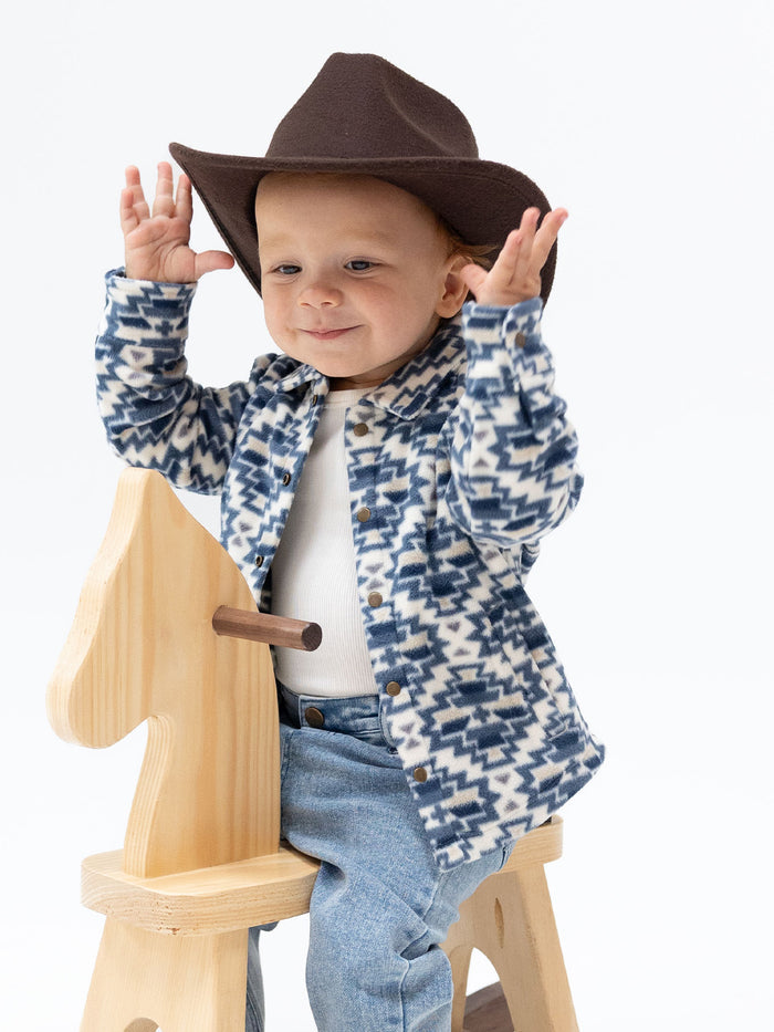 Child in a festive sweater and cowboy hat smiles while playing on a wooden rocking horse.
