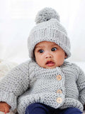Baby wearing a cozy gray knitted sweater and pom-pom hat, looking curiously at the camera.