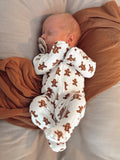 Sleeping baby in a gingerbread-patterned onesie, peacefully cradled on a soft blanket.