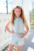 Young girl wearing a denim vest and shorts on a wooden deck.
