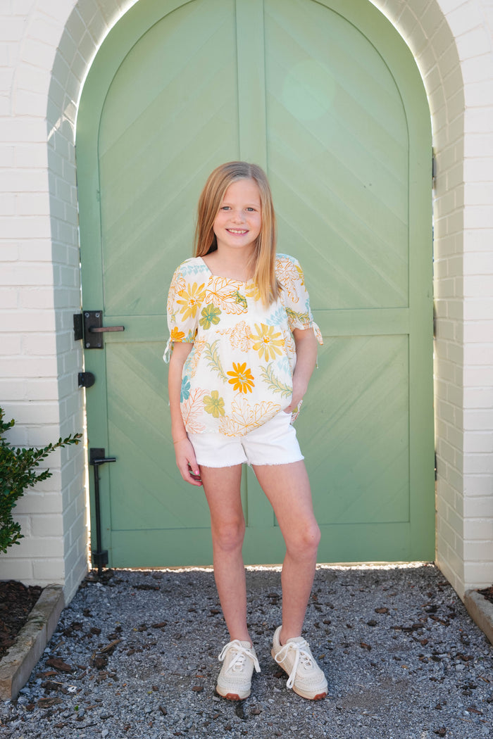 A girl wearing a sleeveless denim top and shorts with a frayed hem.