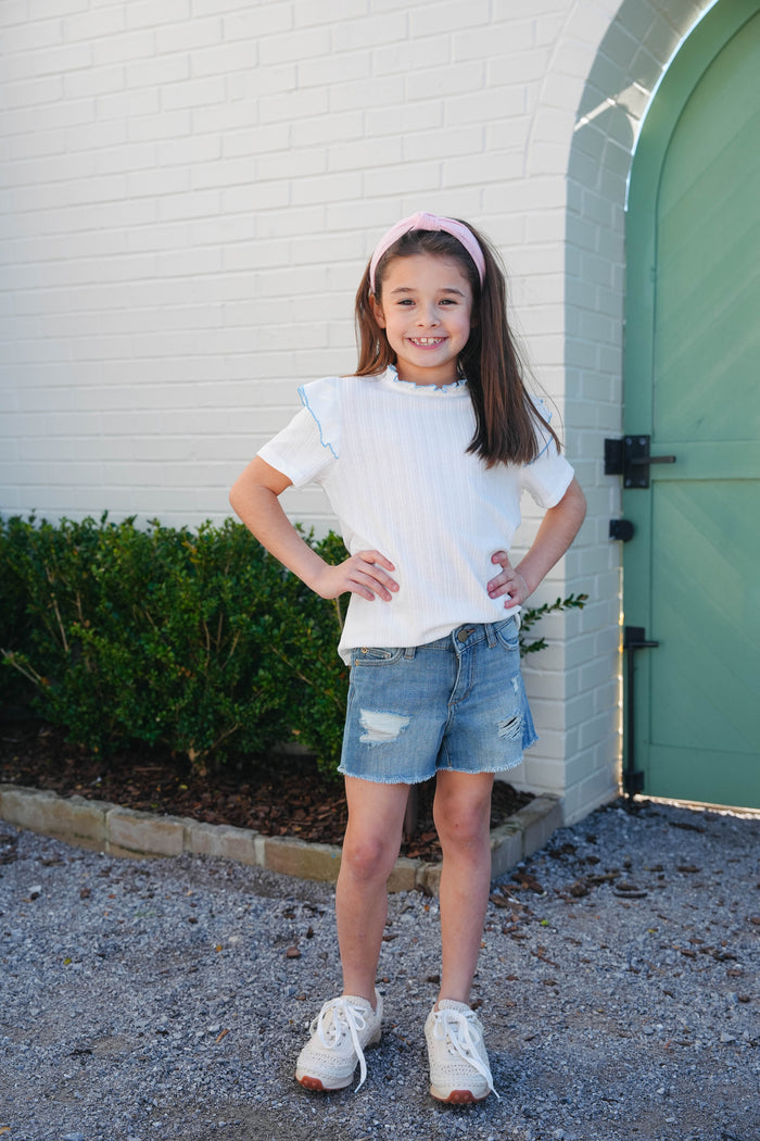 A girl wearing a denim crop top and shorts standing on a wooden deck