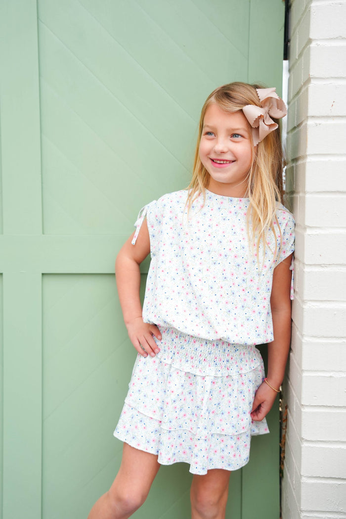 Young girl in a floral outfit standing against a green door.