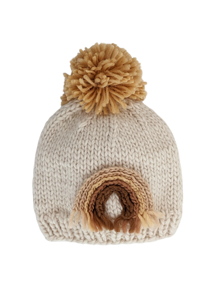 Cream knitted beanie with a brown rainbow design and a fluffy pom-pom on top.