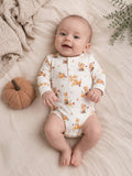 Smiling baby in a printed onesie with foxes, pumpkins, and leaves, resting on a soft blanket. Cozy autumn vibe.