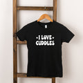 Black t-shirt hanging on a wooden ladder with the text "I LOVE CUDDLES" printed in white.