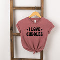 Pink shirt with the text "I LOVE CUDDLES" displayed, hanging on a wooden ladder.