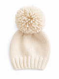 Cream-colored knit beanie with a fluffy pom-pom on top, resting on a white background.