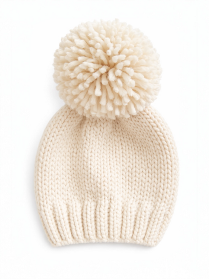 Cream-colored knit beanie with a fluffy pom-pom on top, resting on a white background.