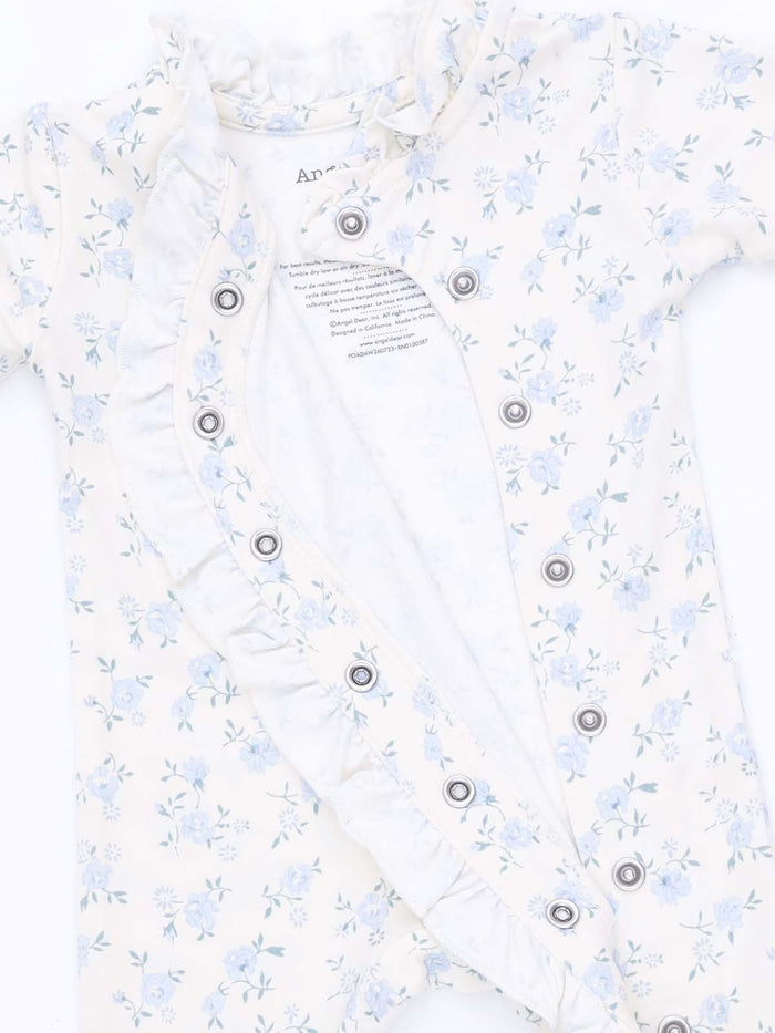 Floral baby onesie in cream with ruffle detailing and snap buttons, partially opened to show the inner lining.