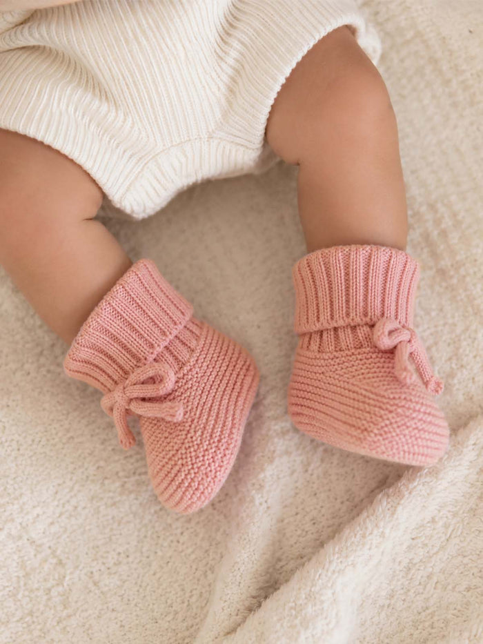 Baby's feet in cozy pink knitted booties on a soft cream blanket.