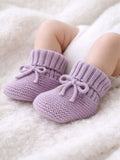 Soft lavender knitted baby booties on a fluffy white blanket, perfect for keeping little feet warm.