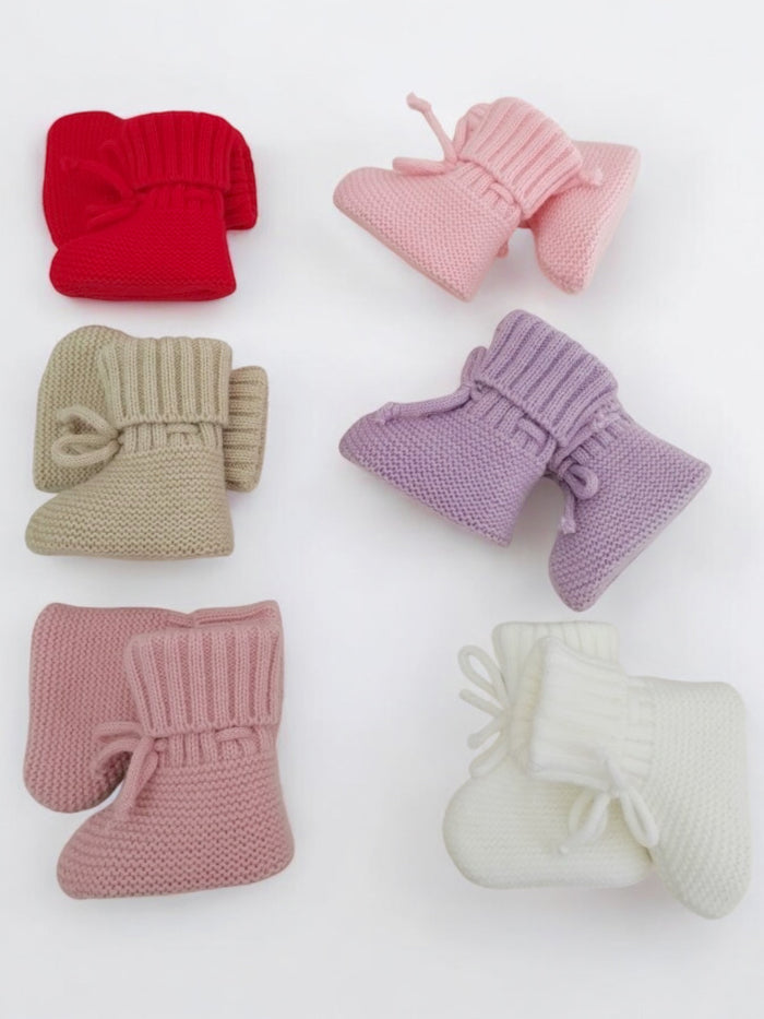Colorful knitted baby booties in red, pink, beige, lavender, and white arranged on a light surface.