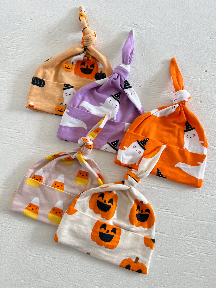 Five festive baby hats in seasonal colors featuring pumpkins, ghosts, and candy corn patterns.