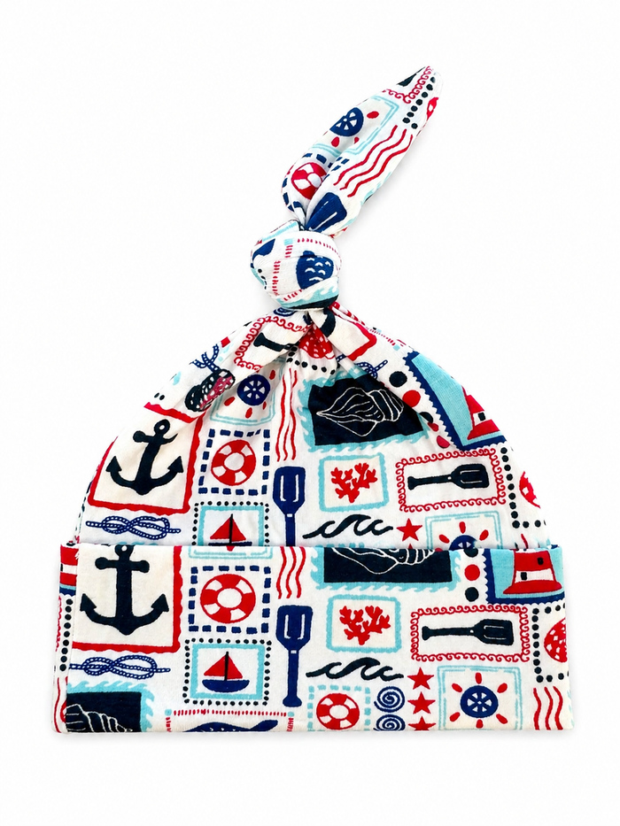 Nautical-themed baby hat featuring anchors, boats, and ocean symbols in red, blue, and white colors.