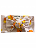 Light pink baby headband with a large bow and candy corn pattern, labeled for ages 0-6 months.