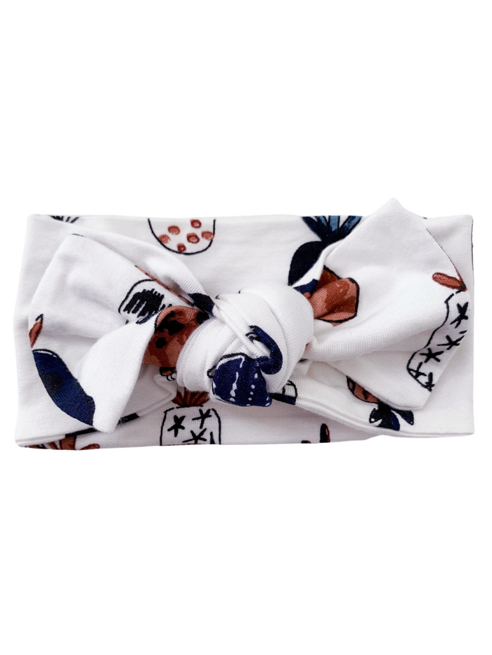 White headband with a knotted design, featuring colorful fruit and floral patterns.
