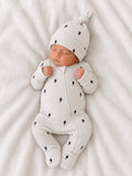 Newborn baby in a light gray outfit with lightning bolt patterns, peacefully sleeping on a soft blanket.