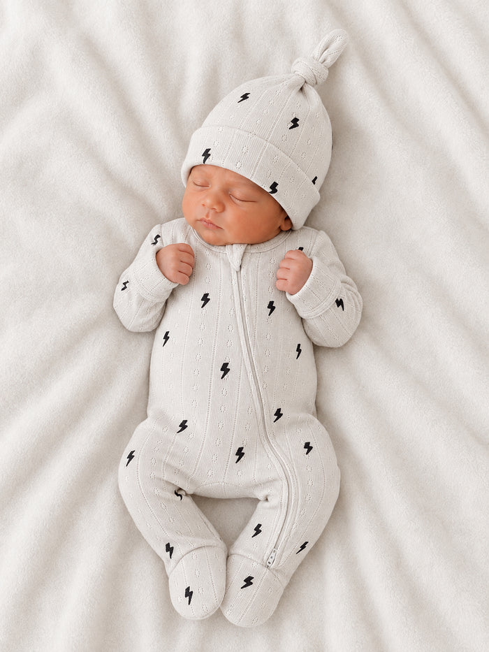 Newborn baby in a light gray outfit with lightning bolt patterns, peacefully sleeping on a soft blanket.
