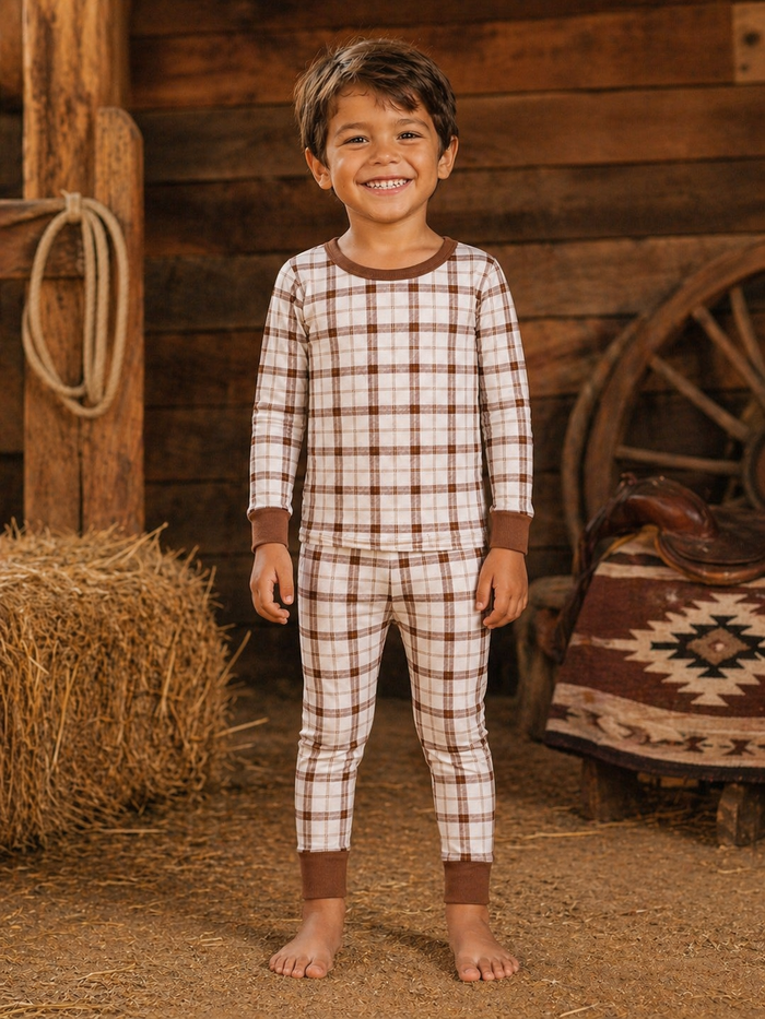 Smiling boy in brown and white plaid pajamas standing on a farm with hay and rustic decor.