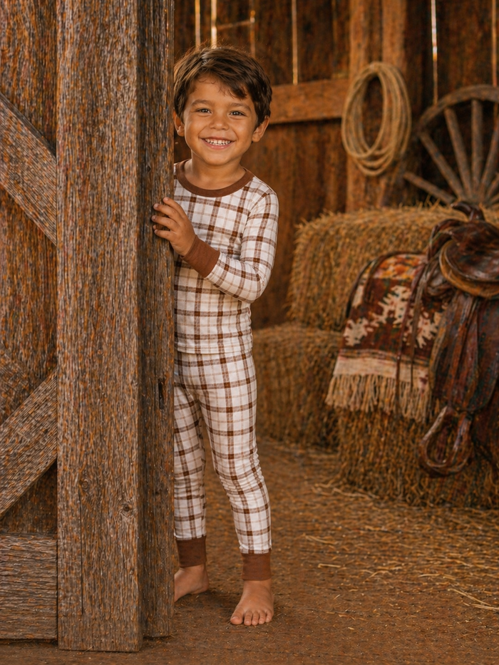 Smiling child in plaid pajamas peeking from a barn door, surrounded by hay bales and rustic decor.