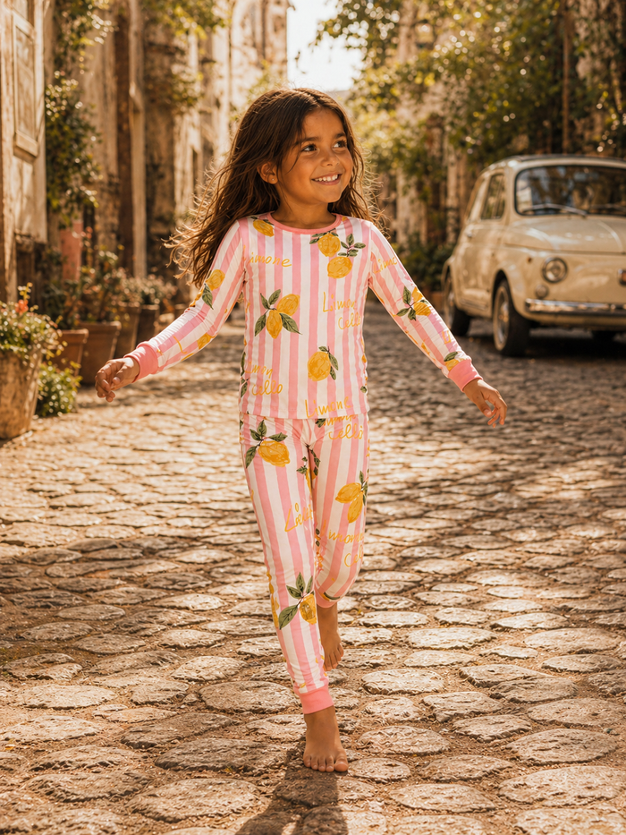 Girl in lemon-themed pajamas walking on a cobblestone path with greenery and a vintage car in the background.