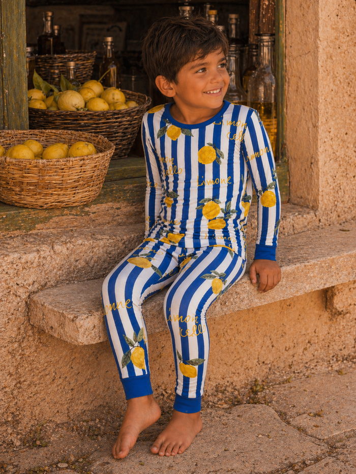 Boy in striped blue and white pajamas with lemons, sitting on a stone step next to a basket of lemons.