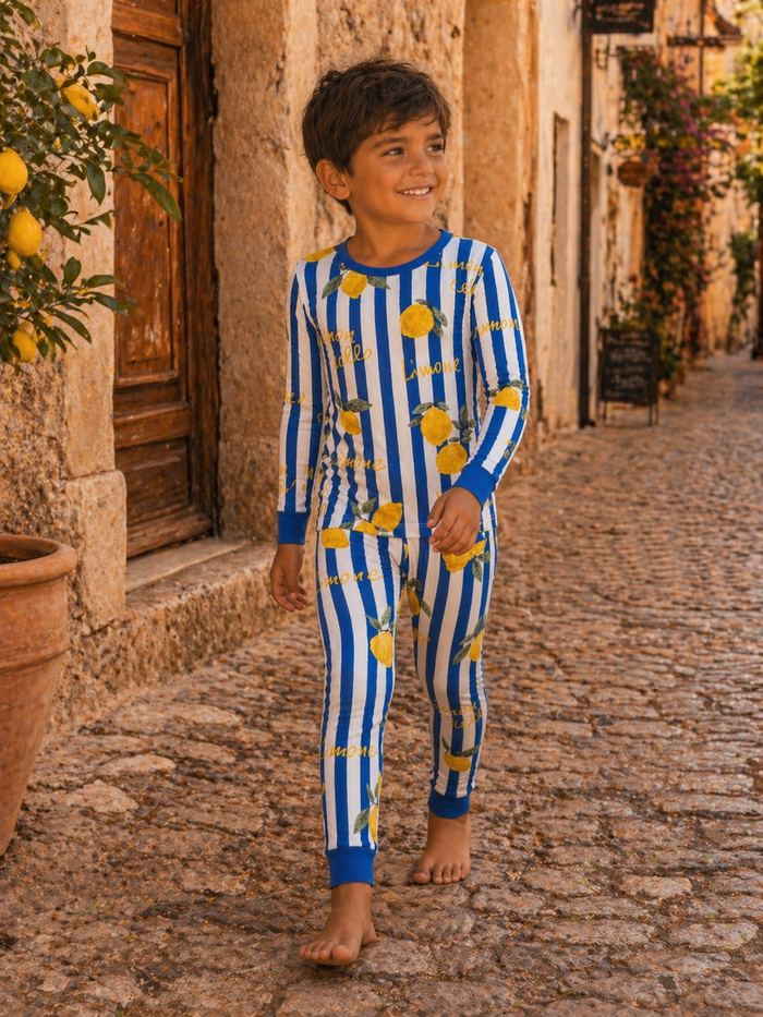 Smiling child wearing blue and white striped pajamas with lemon patterns, walking on a cobblestone street.