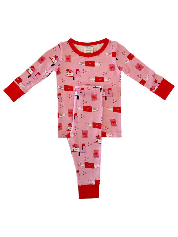 Pink pajamas with red accents featuring a playful mail theme and whimsical envelopes printed throughout.