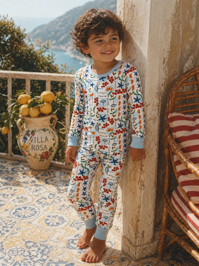 Smiling child in colorful pajamas stands on a balcony with lemons, overlooking a scenic view.