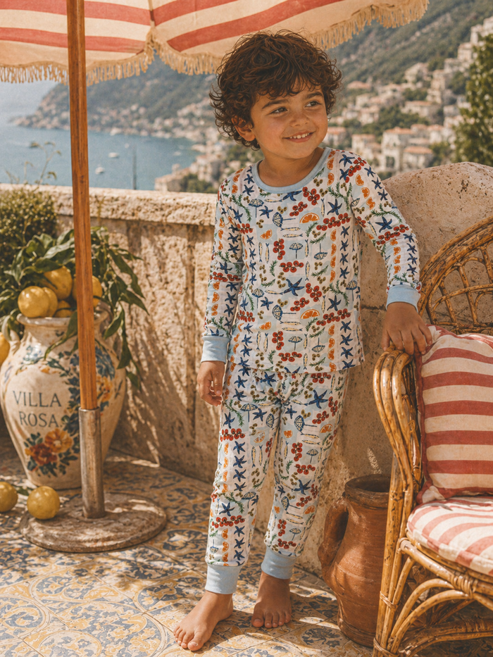 Child in vibrant, patterned pajamas smiles beside a decorative umbrella and planter in a sunny outdoor setting.
