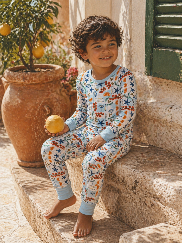 Young boy in colorful pajamas sitting on steps, holding a lemon, surrounded by greenery and a pottery planter.