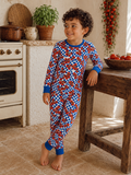 Smiling child in colorful pajamas, standing by a rustic kitchen with tomatoes and plants in warm lighting.