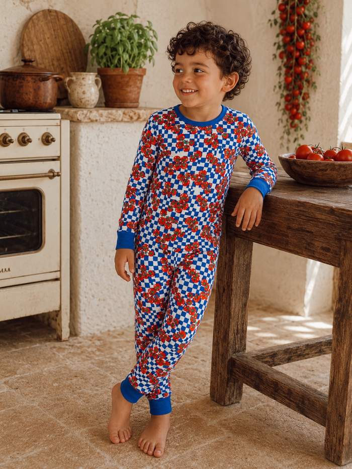 Smiling child in colorful pajamas, standing by a rustic kitchen with tomatoes and plants in warm lighting.