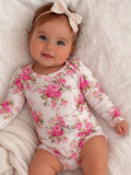 Smiling baby girl in a floral onesie with a bow, lying on a soft blanket.