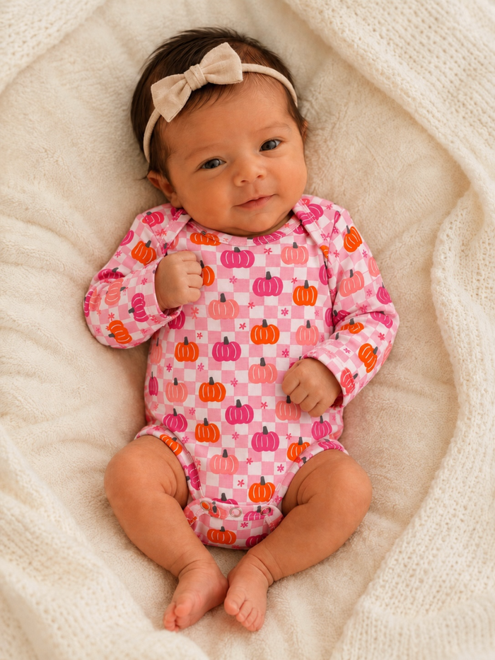 Smiling baby in a pink pumpkin-patterned onesie, laying on a soft, cream-colored blanket.