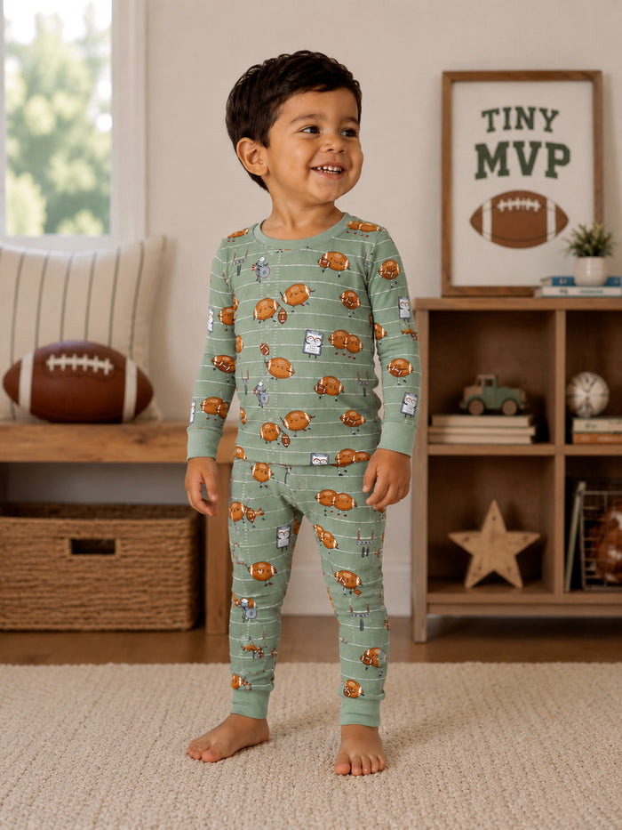 Smiling child in printed pajamas with playful designs, standing in a cozy living room with a football and decor.