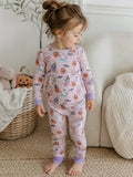 Toddler in Halloween-themed pajamas with pumpkins and ghosts, standing beside a cozy basket and plush toys.