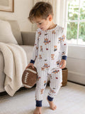 Young boy in playful pajamas with teddy bears, holding a decorative football in a cozy living room setting.
