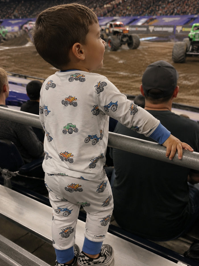 Child in monster truck pajamas watching a monster truck show from the stands, with excited audience in background.