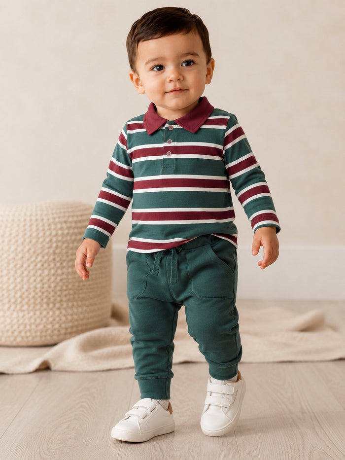Toddler wearing a striped long-sleeve polo and green joggers, walking on wood floor with a neutral background.